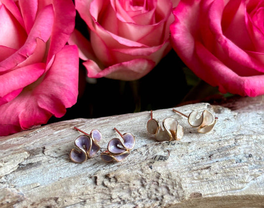 Pair of gold earrings on a wooden surface with pink roses in the background