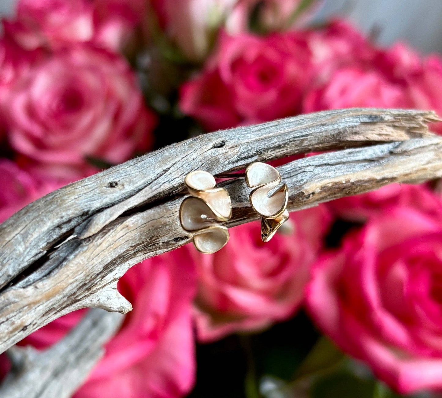Gold earrings on a branch with pink roses in the background