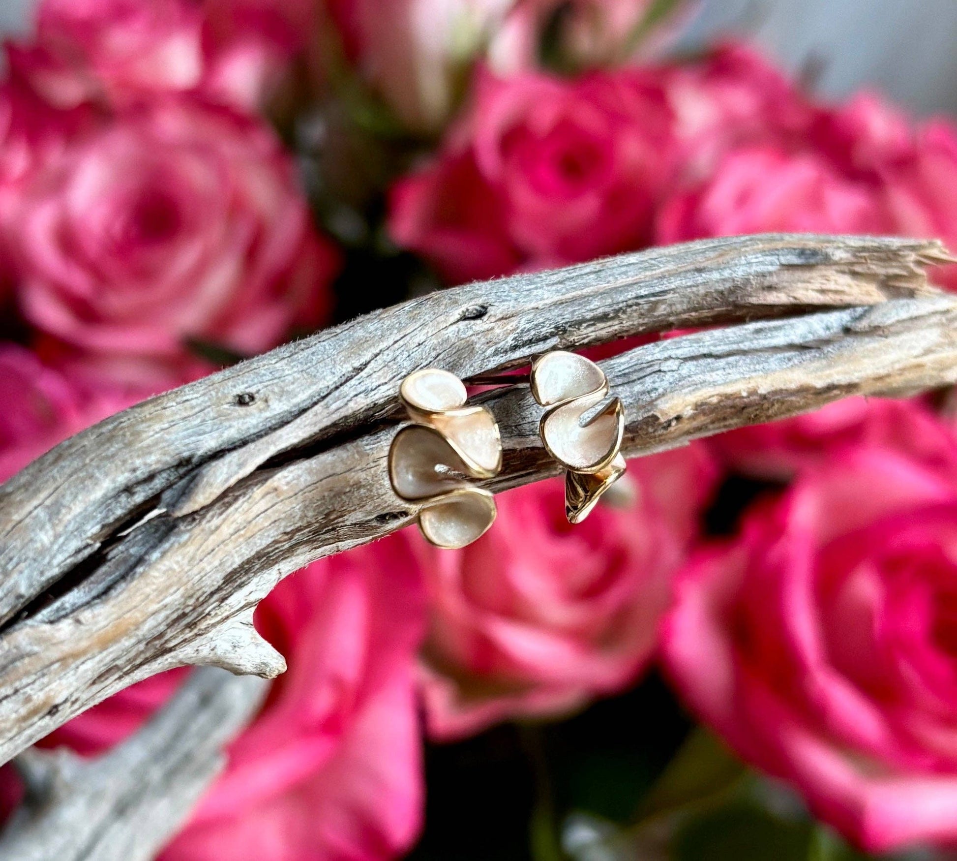 Gold earrings on a branch with pink roses in the background
