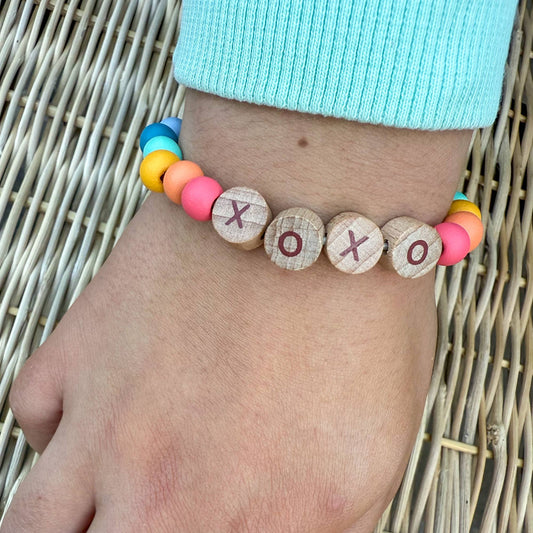 Colorful bracelet with wooden beads spelling 'XO' on a wrist against a woven background