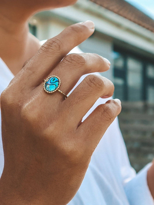 Close-up of a hand wearing a ring with a blue gemstone, blurred background