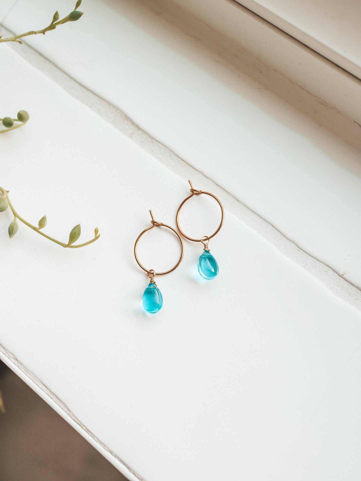 Gold earrings with blue teardrop beads on a white surface