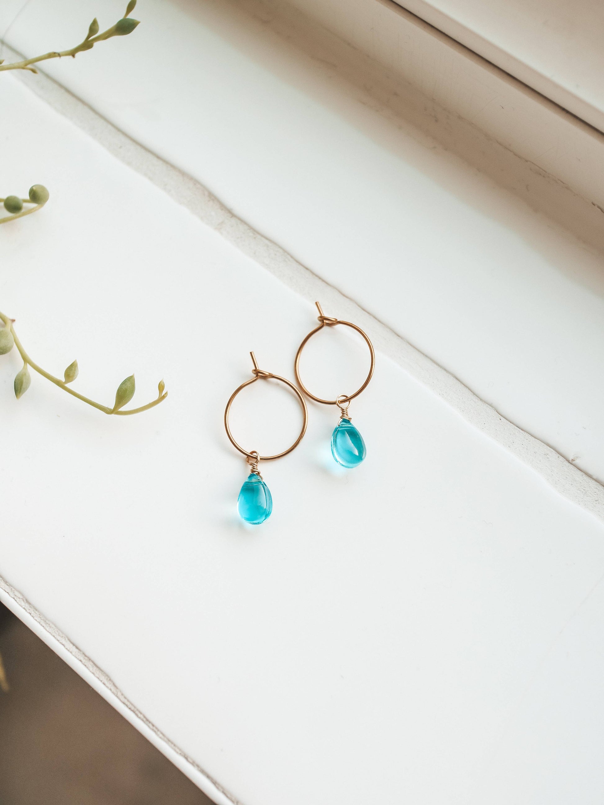 Gold earrings with blue teardrop beads on a white surface