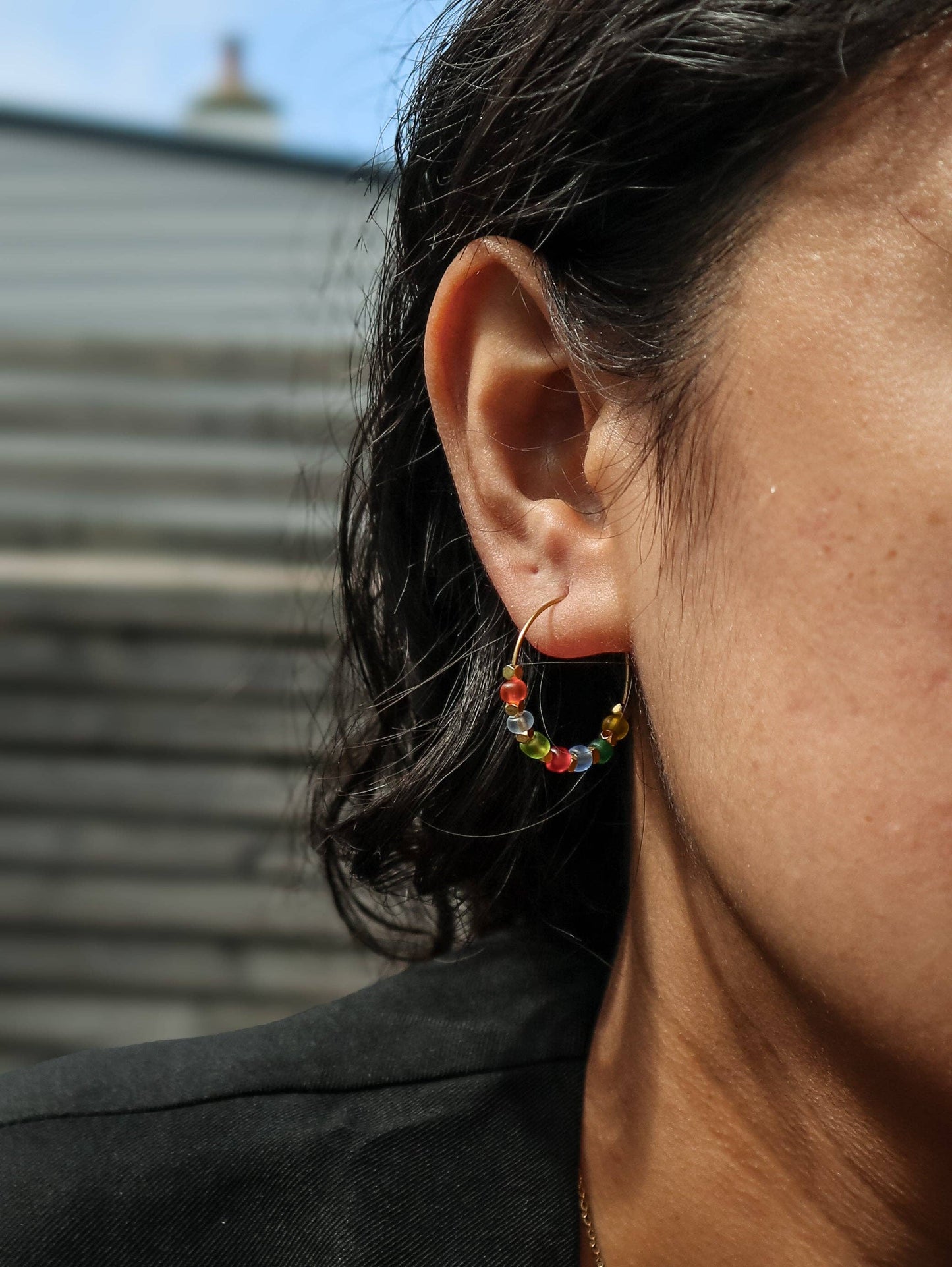 Close-up of an ear wearing a colorful hoop earring with a blurred background