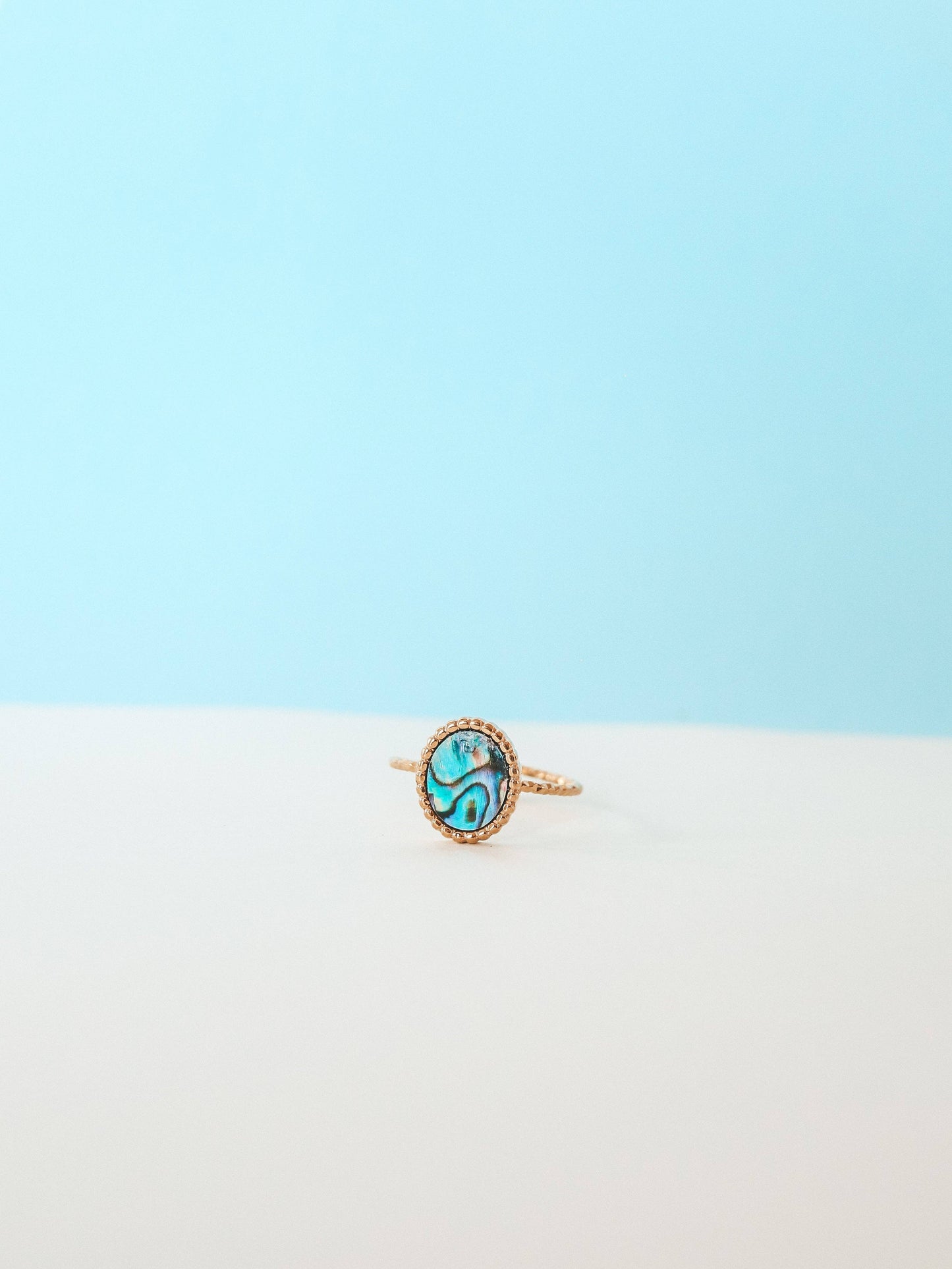 Gold ring with a green gemstone on a light blue and white gradient background