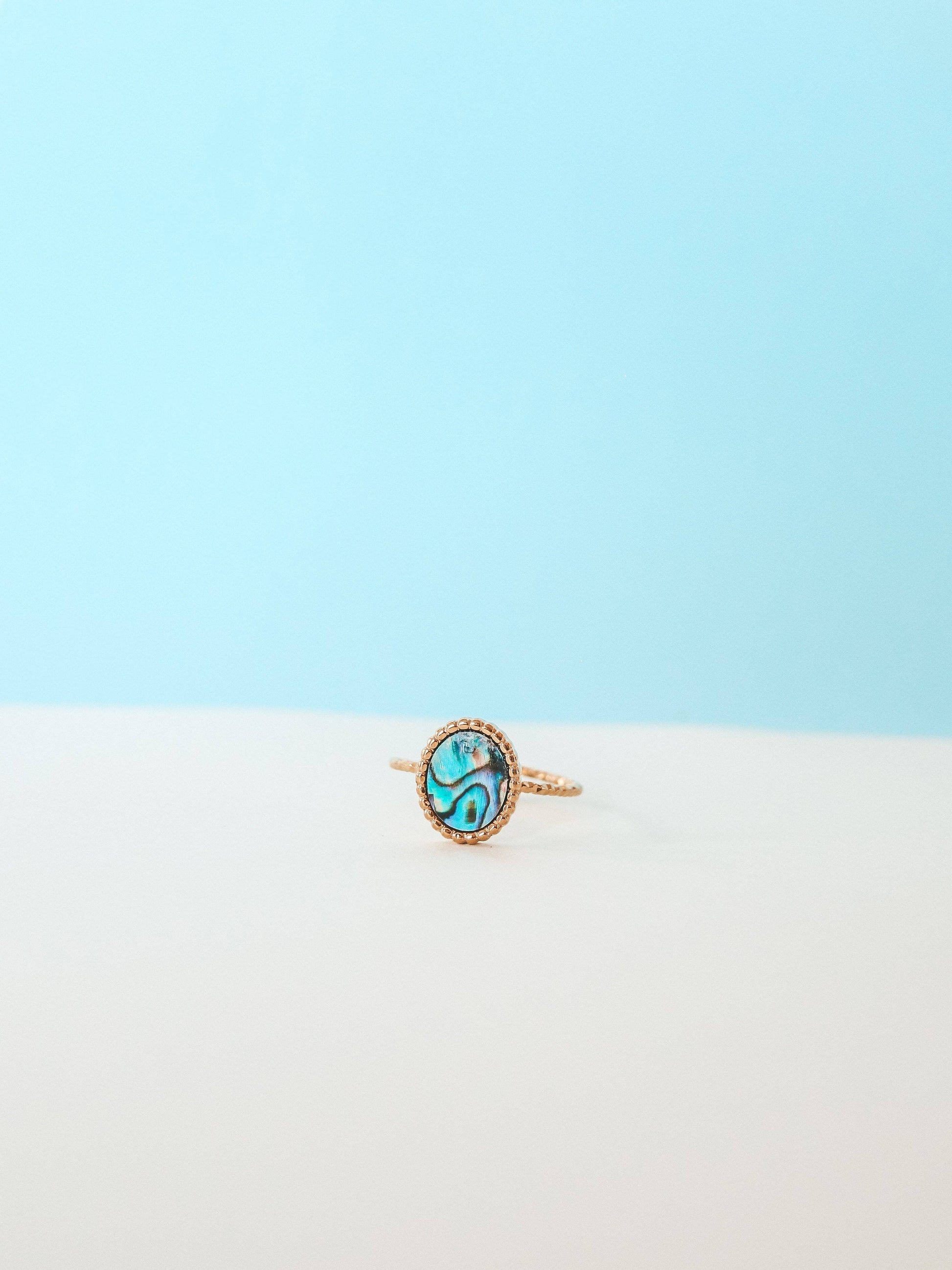 Gold ring with a green gemstone on a light blue and white gradient background