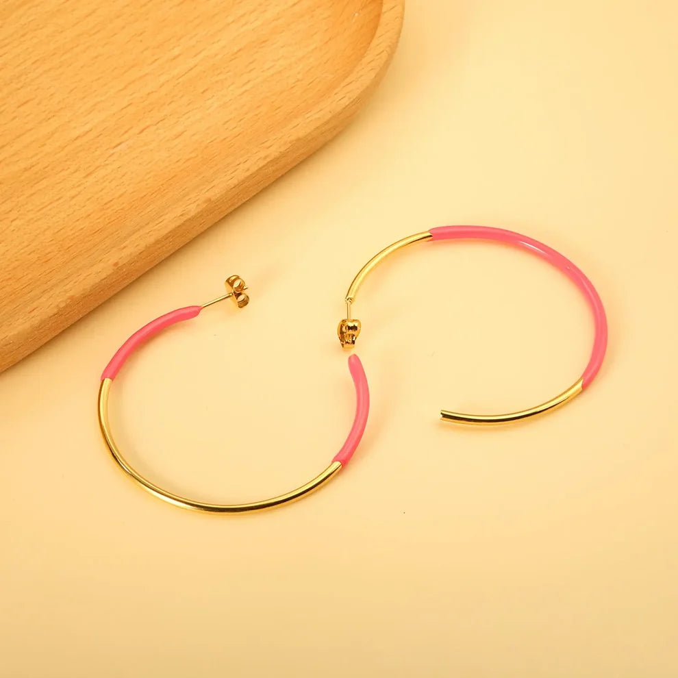 Gold and pink hoop earrings displayed on a warm beige surface next to a wooden tray.