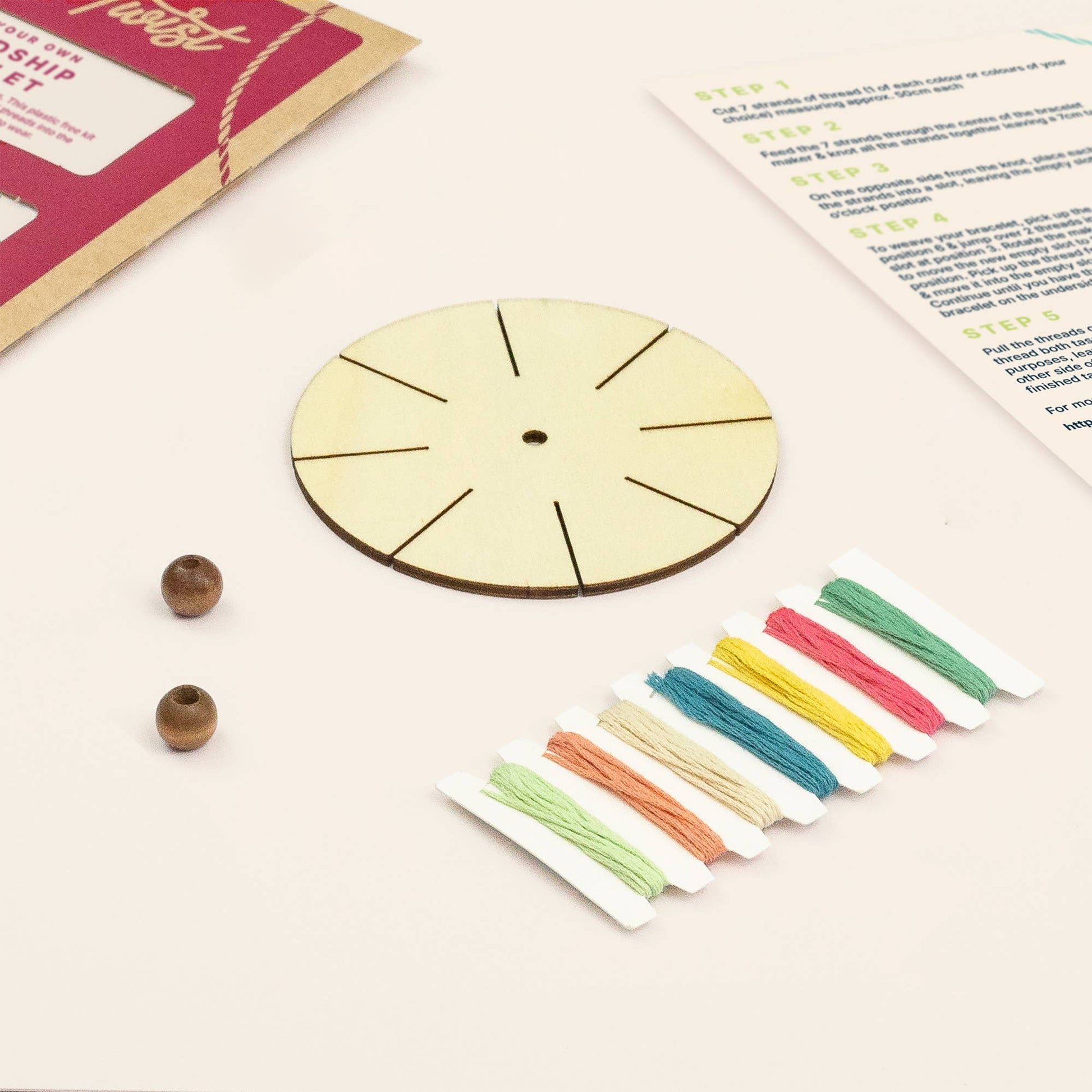 Wooden bracelet-making kit with beads and colorful strings on a light surface