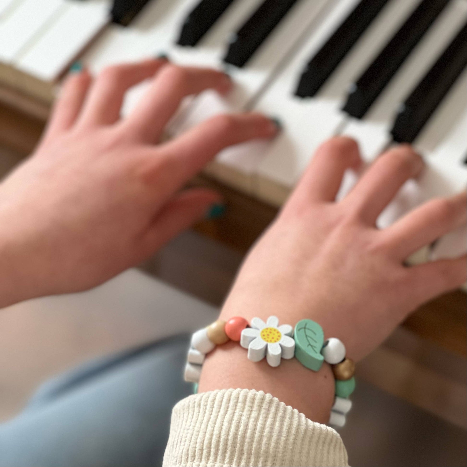 Close-up of hands playing a piano with a colorful bracelet on the wrist.