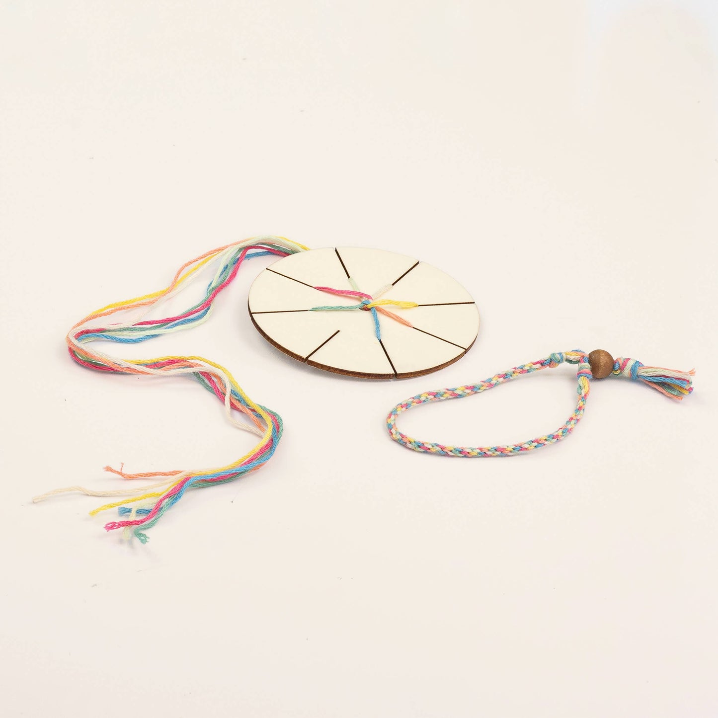 Colorful braided bracelet with a wooden beading tool on a light background