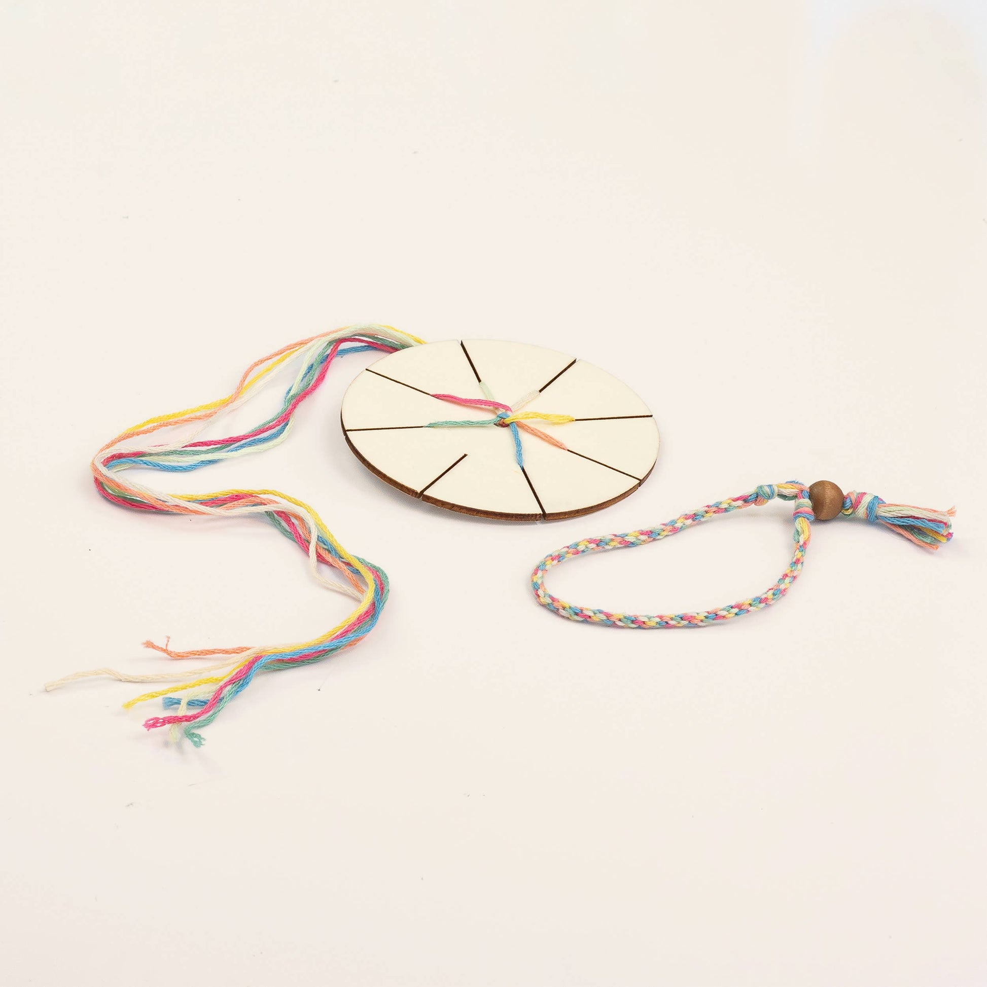 Colorful braided bracelet with a wooden beading tool on a light background