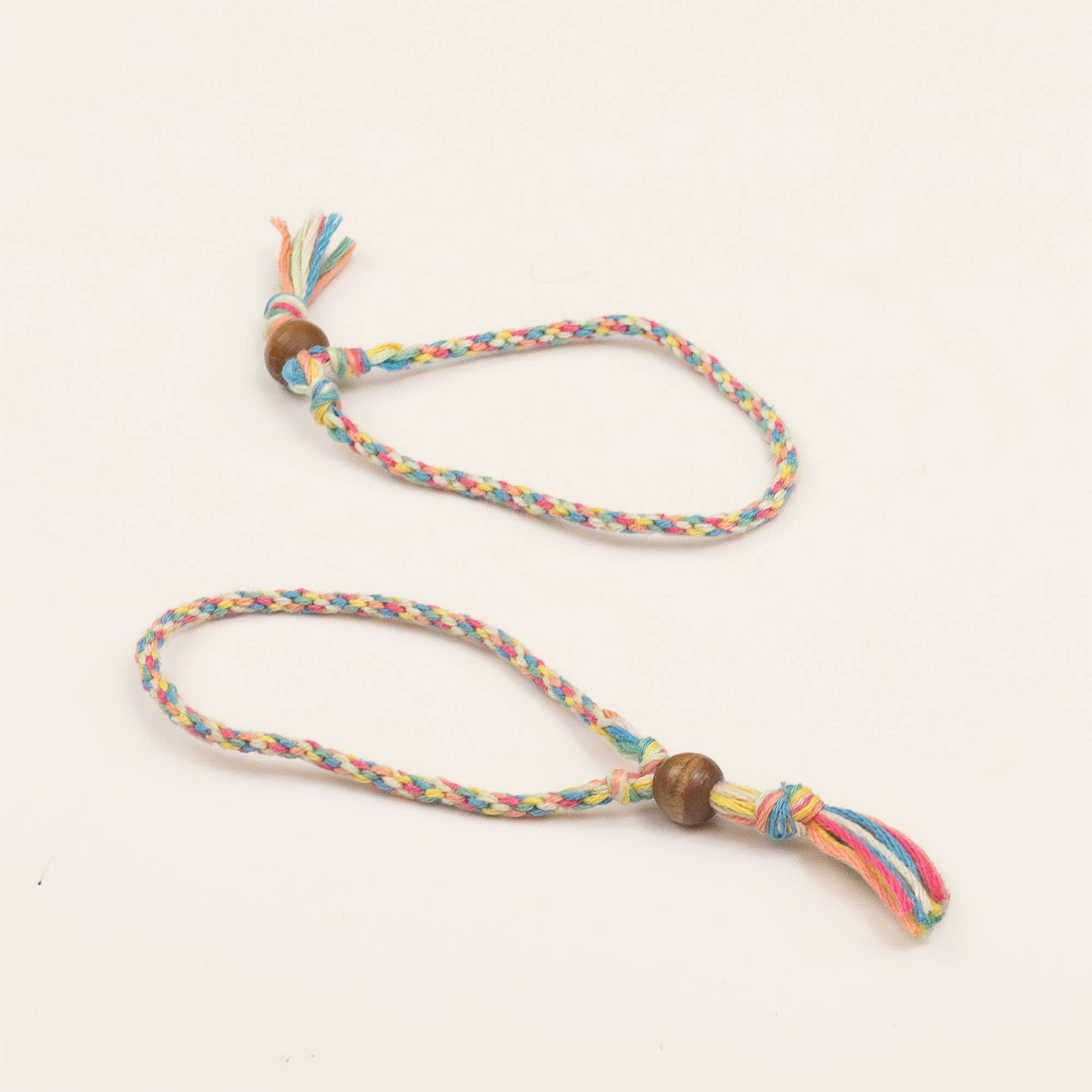 Colorful braided dog toy with wooden beads on a light beige background