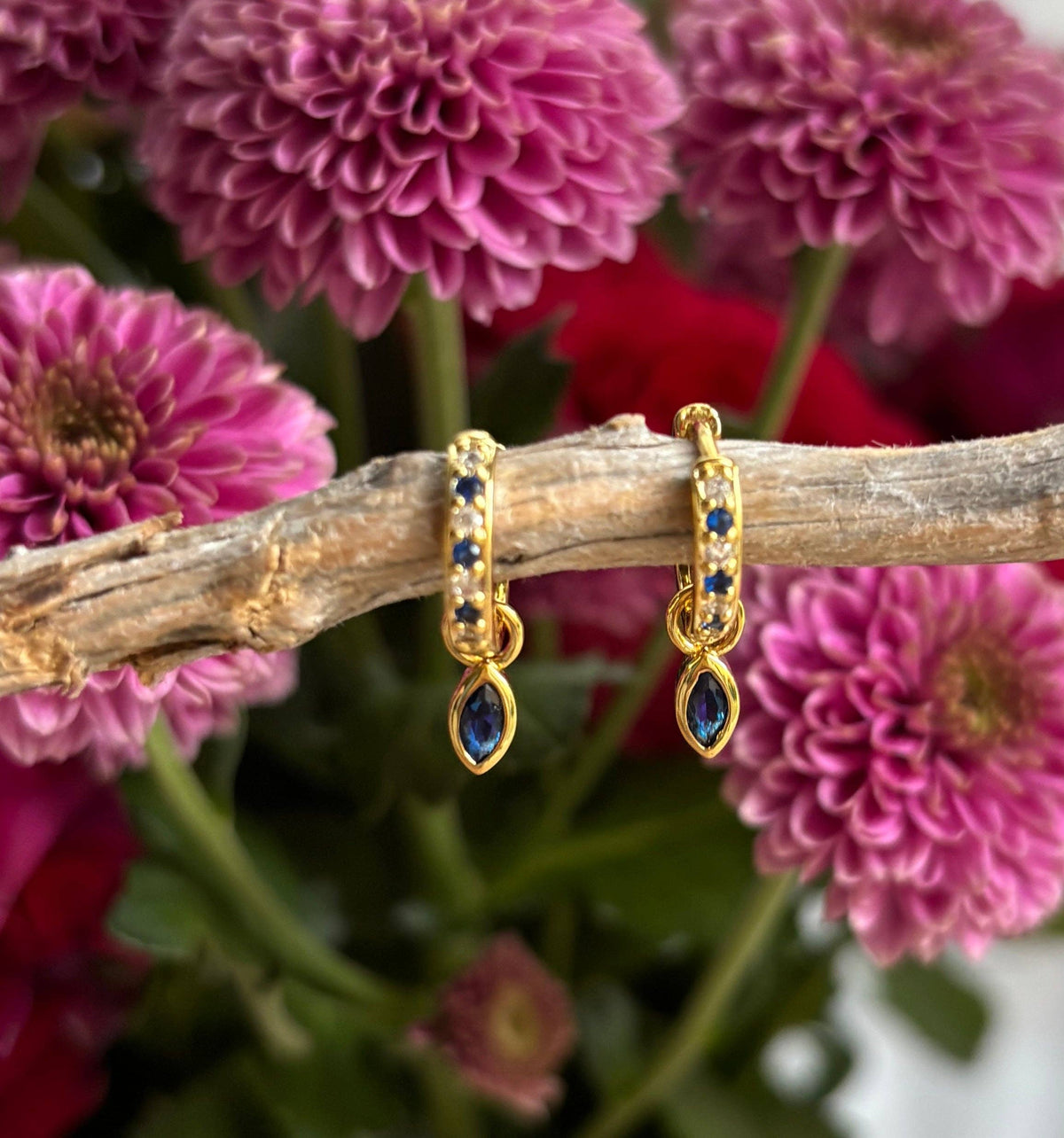 Gold earrings with blue stones on a branch with pink flowers