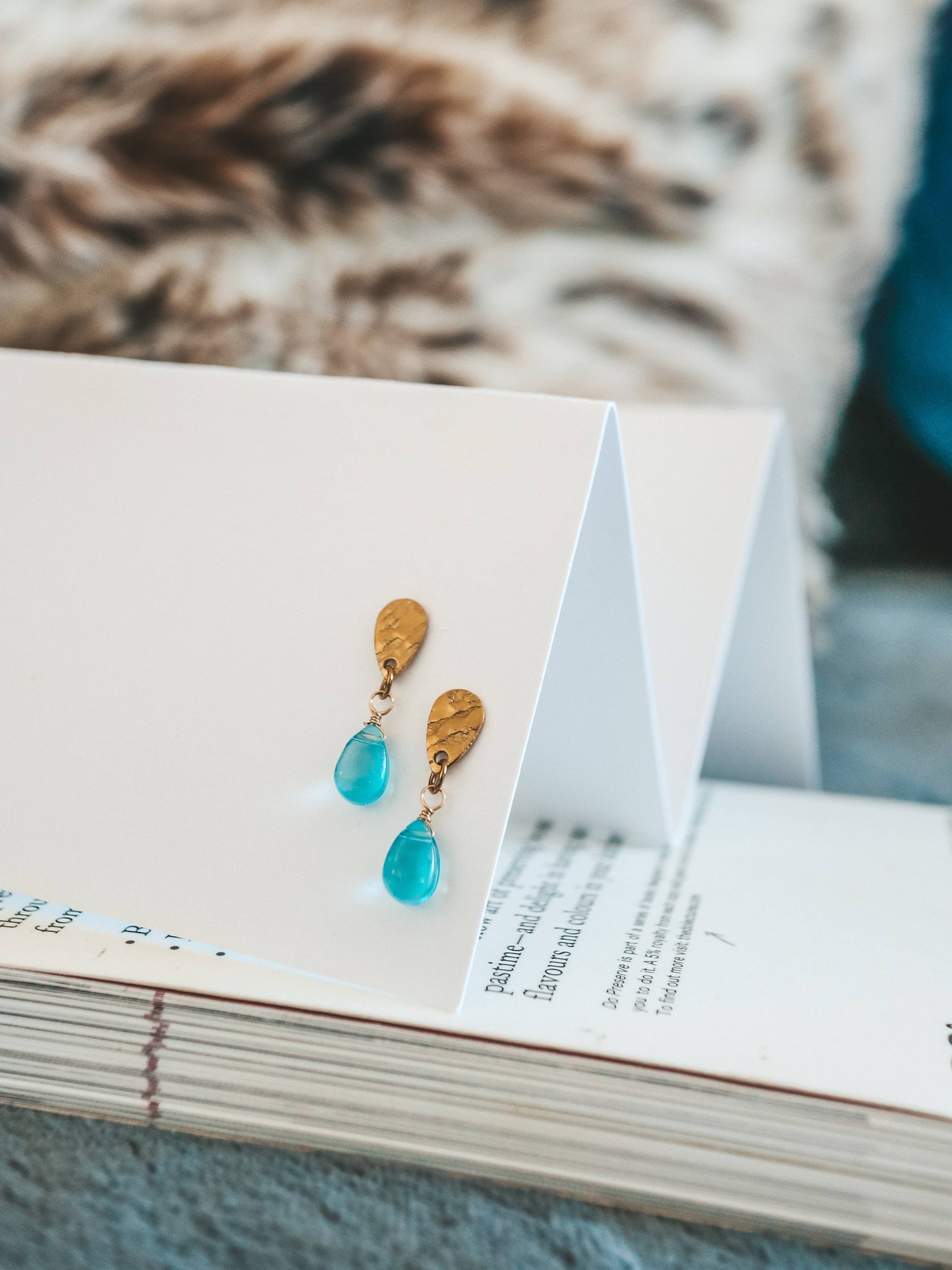 Pair of turquoise teardrop earrings on a white card with a blurred background