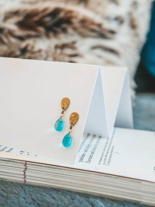 Pair of turquoise teardrop earrings on a white card with a blurred background