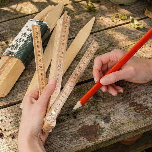 A close-up of hands using traditional wooden measuring rulers with Chinese characters to mark a red pencil on a rustic wooden table outdoors.