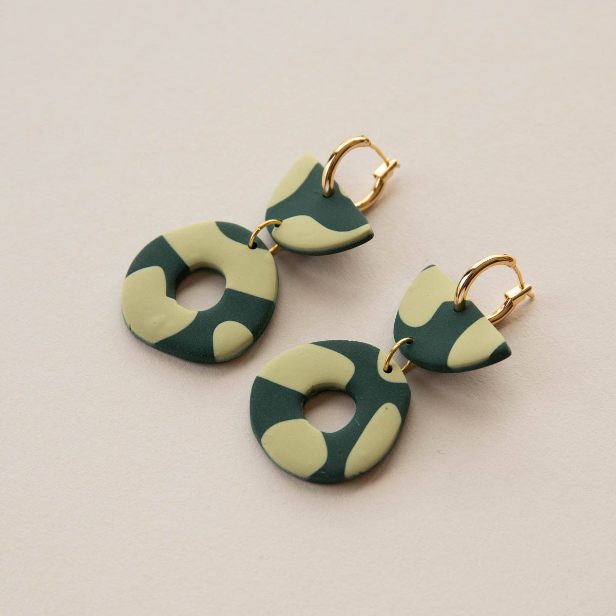Green and beige patterned earrings on a light beige background