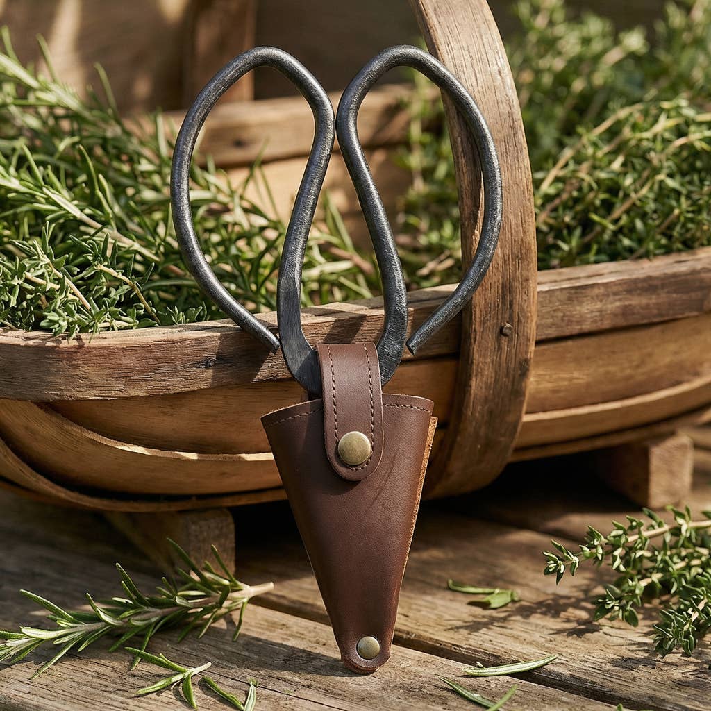 Shears with a leather sheath on a wooden surface with greenery