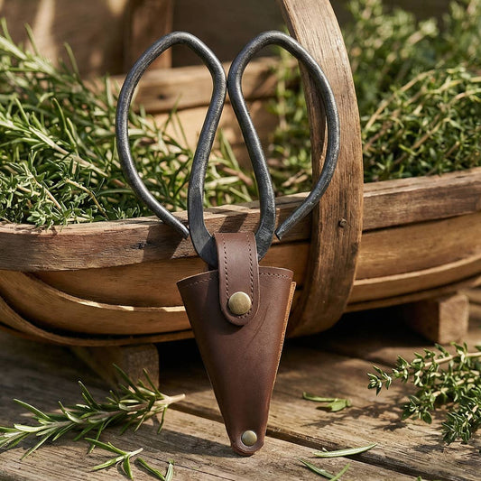 Shears with a leather sheath on a wooden surface with greenery