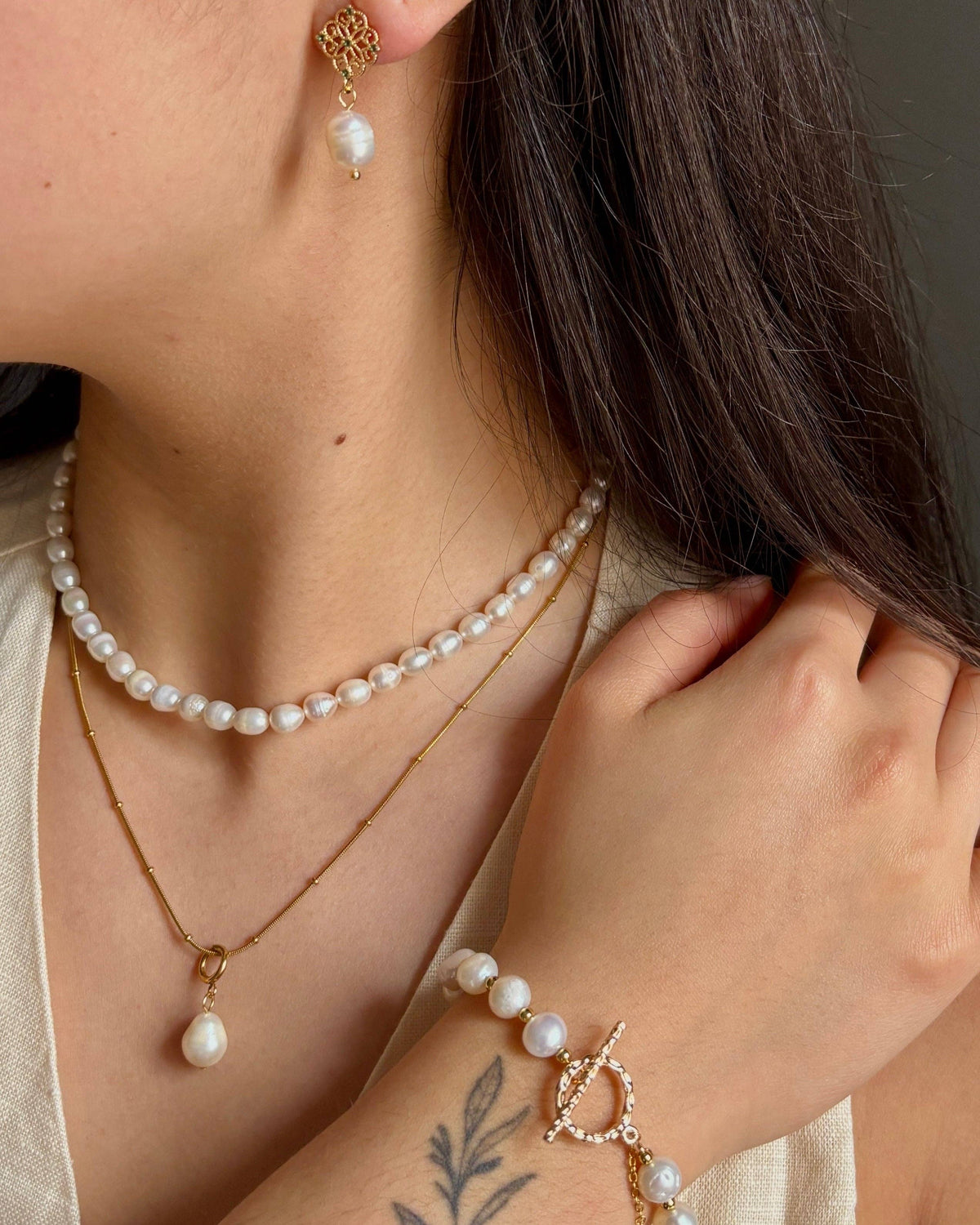 Pearl necklace, earrings, and bracelet on a person against a neutral background