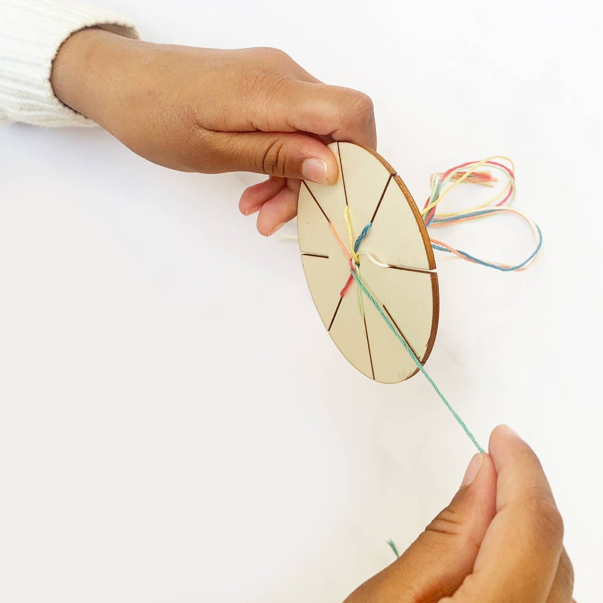 Person holding a circular wooden tool with string, on a white background
